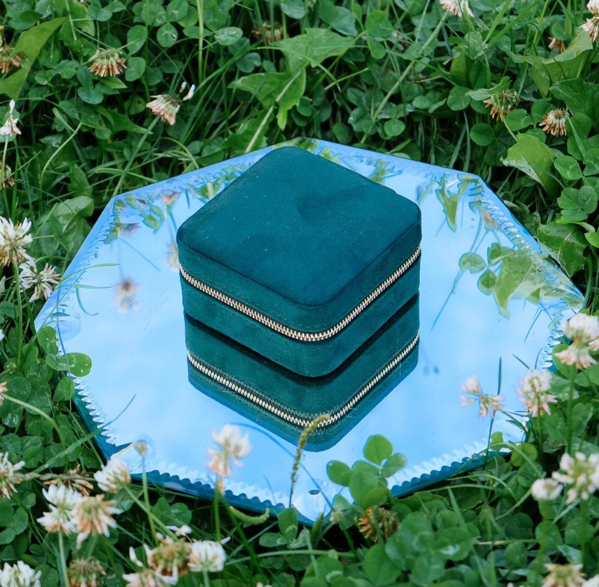 Gesloten groene velours reissieradendoos van Maison Scarlett op een blauw dienblad in het gras